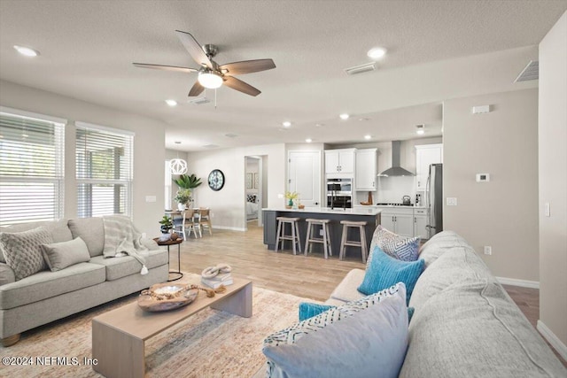 living room with a textured ceiling, light wood-type flooring, and ceiling fan