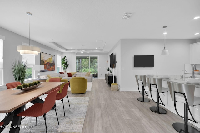 dining space with a tray ceiling, ceiling fan, and light hardwood / wood-style flooring