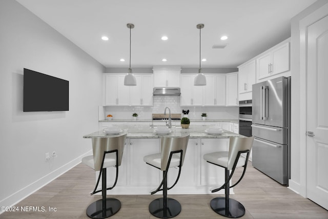 kitchen featuring light wood-type flooring, a kitchen island with sink, white cabinets, hanging light fixtures, and appliances with stainless steel finishes