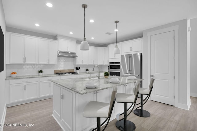 kitchen with appliances with stainless steel finishes, decorative light fixtures, an island with sink, and white cabinets