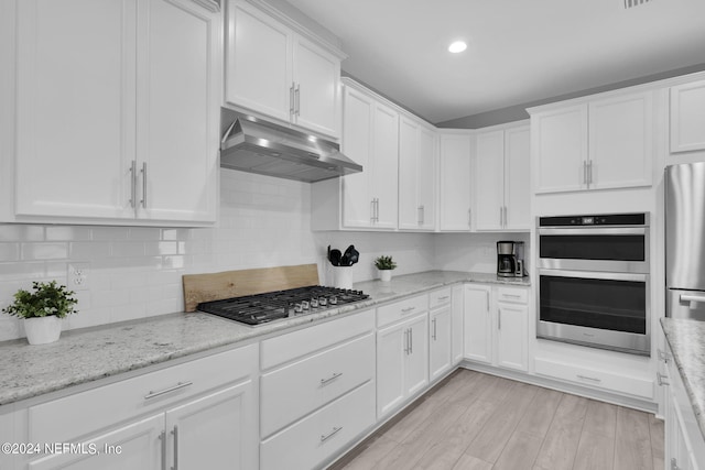 kitchen with light wood-type flooring, white cabinets, decorative backsplash, stainless steel appliances, and light stone countertops