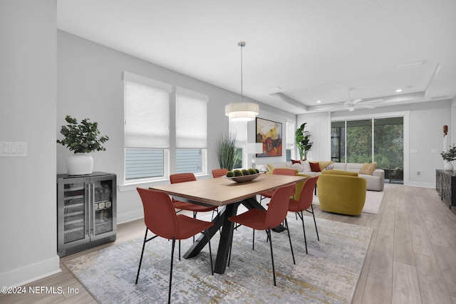 dining room featuring a healthy amount of sunlight, a raised ceiling, light hardwood / wood-style floors, and beverage cooler