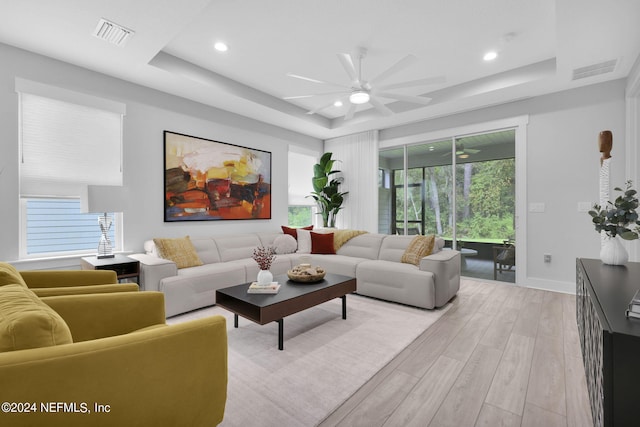 living room featuring ceiling fan, light hardwood / wood-style flooring, and a raised ceiling