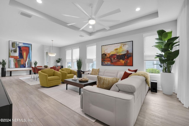 living room featuring light wood-type flooring, a tray ceiling, ceiling fan, and a wealth of natural light