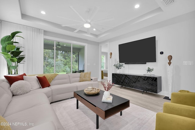 living room with ceiling fan, a raised ceiling, and light hardwood / wood-style floors