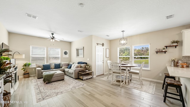 living room with ceiling fan with notable chandelier, a textured ceiling, light hardwood / wood-style flooring, and a healthy amount of sunlight