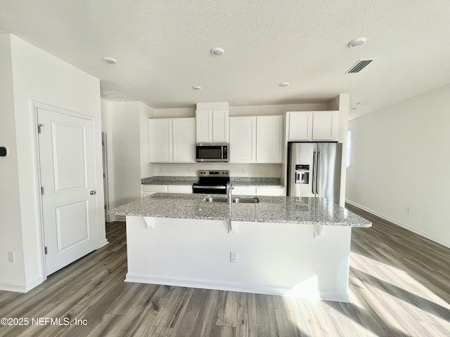 kitchen with stainless steel appliances, white cabinetry, and an island with sink