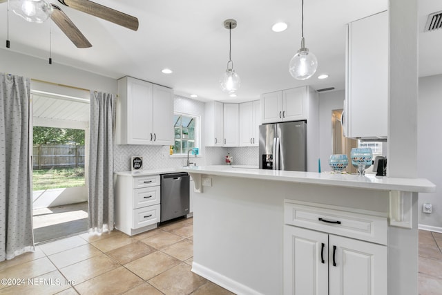 kitchen with appliances with stainless steel finishes, hanging light fixtures, white cabinetry, and plenty of natural light