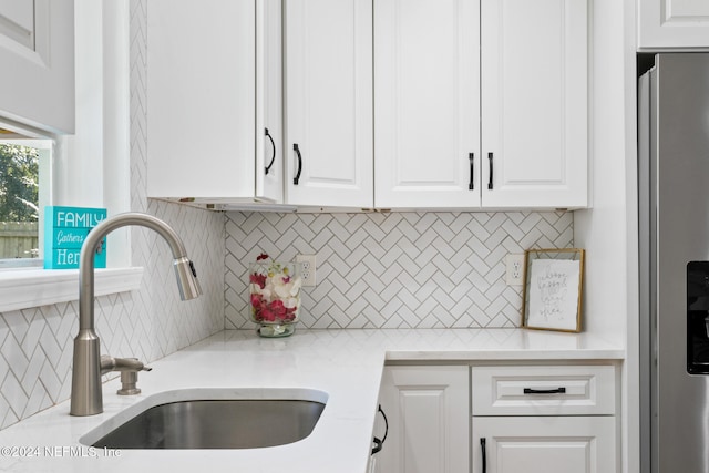 kitchen featuring sink, white cabinetry, stainless steel refrigerator with ice dispenser, and backsplash