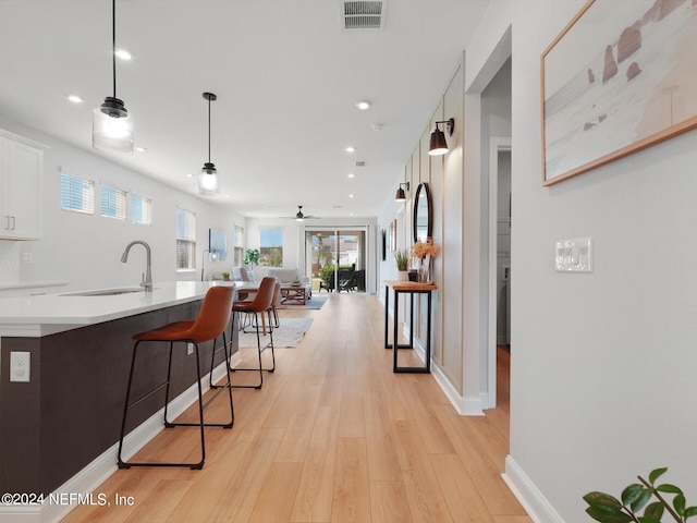 kitchen with hanging light fixtures, a kitchen breakfast bar, white cabinetry, light wood-type flooring, and sink