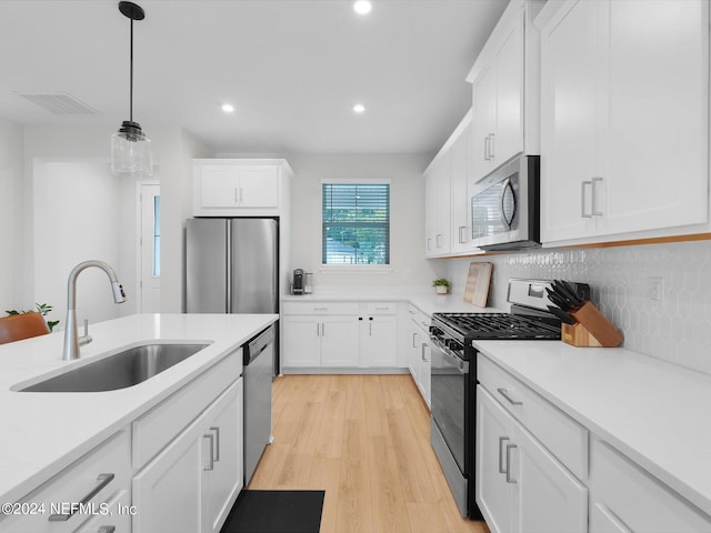 kitchen featuring appliances with stainless steel finishes, sink, light wood-type flooring, decorative light fixtures, and white cabinets