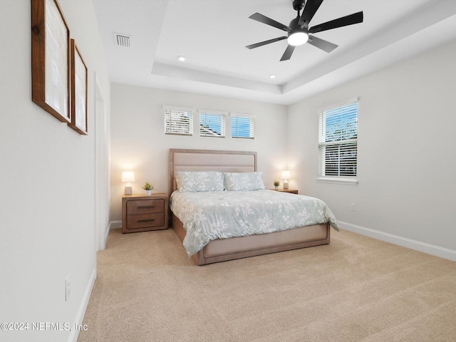 carpeted bedroom with a raised ceiling and ceiling fan