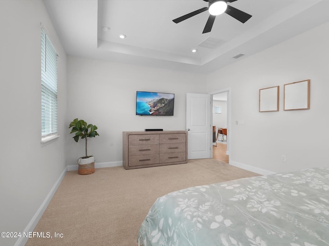 bedroom with light colored carpet, a raised ceiling, and ceiling fan