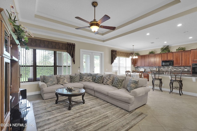 tiled living room featuring ornamental molding, a raised ceiling, and ceiling fan with notable chandelier