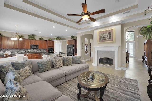 living room featuring ceiling fan with notable chandelier, light tile patterned flooring, a tray ceiling, and ornamental molding