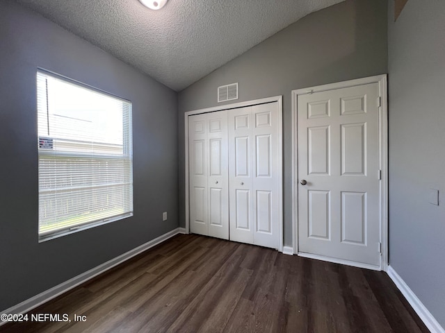 unfurnished bedroom with vaulted ceiling, multiple windows, a textured ceiling, and dark hardwood / wood-style flooring