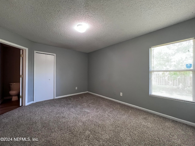 unfurnished bedroom with connected bathroom, a closet, a textured ceiling, and carpet floors