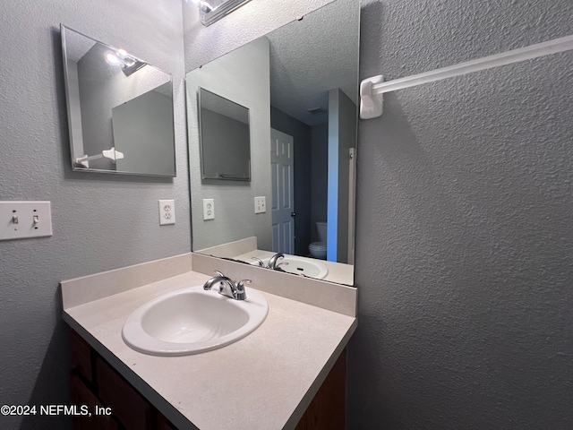 bathroom featuring toilet, a textured ceiling, and vanity