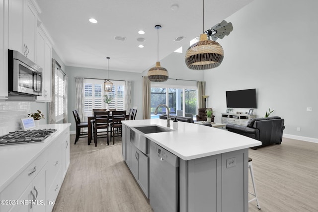 kitchen with appliances with stainless steel finishes, hanging light fixtures, white cabinetry, a center island with sink, and sink