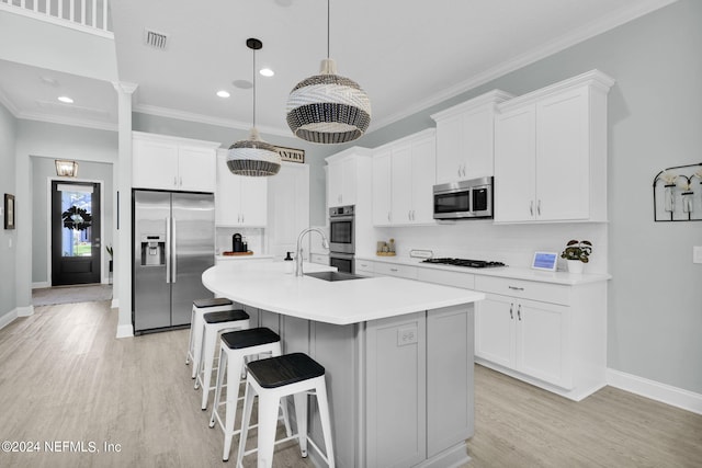 kitchen featuring sink, white cabinetry, hanging light fixtures, stainless steel appliances, and a center island with sink