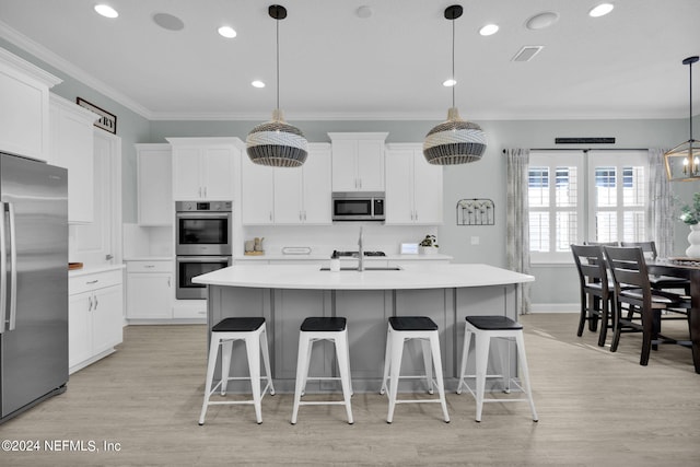 kitchen featuring white cabinets, an island with sink, decorative light fixtures, appliances with stainless steel finishes, and light wood-type flooring