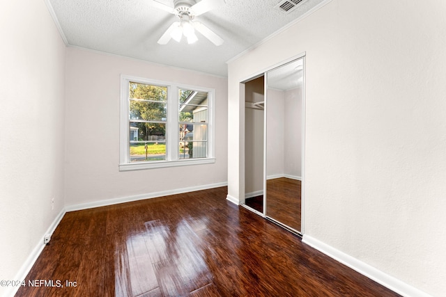 unfurnished bedroom with dark hardwood / wood-style flooring, a closet, a textured ceiling, crown molding, and ceiling fan