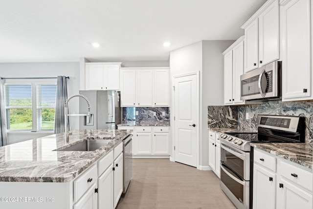 kitchen featuring light stone counters, white cabinetry, appliances with stainless steel finishes, and a kitchen island with sink