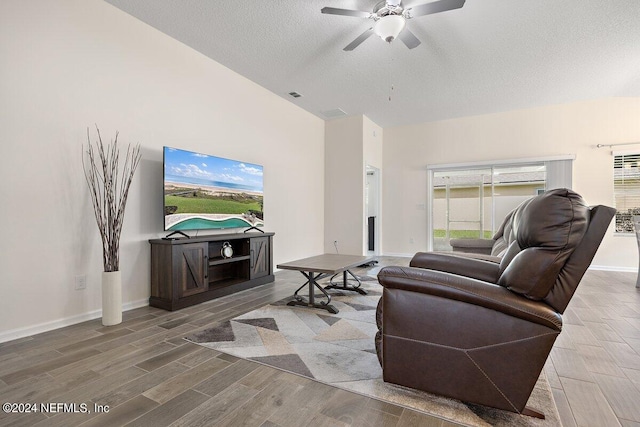 living room with wood-type flooring, lofted ceiling, ceiling fan, and a textured ceiling