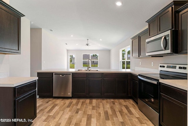 kitchen featuring light wood-style flooring, stainless steel appliances, a peninsula, a sink, and light countertops