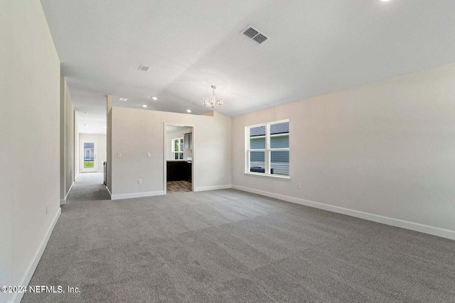 carpeted empty room featuring a chandelier, visible vents, vaulted ceiling, and baseboards