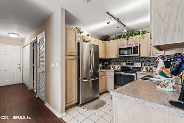 kitchen with light brown cabinets, light hardwood / wood-style flooring, stainless steel appliances, rail lighting, and tasteful backsplash