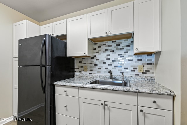 kitchen with black fridge, white cabinetry, sink, and tasteful backsplash