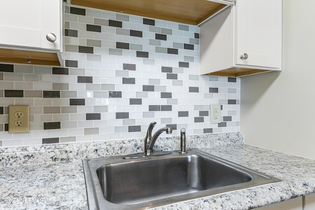 kitchen featuring white cabinets, backsplash, light stone countertops, and sink