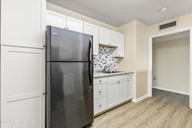 kitchen featuring sink, light hardwood / wood-style flooring, tasteful backsplash, white cabinetry, and stainless steel refrigerator