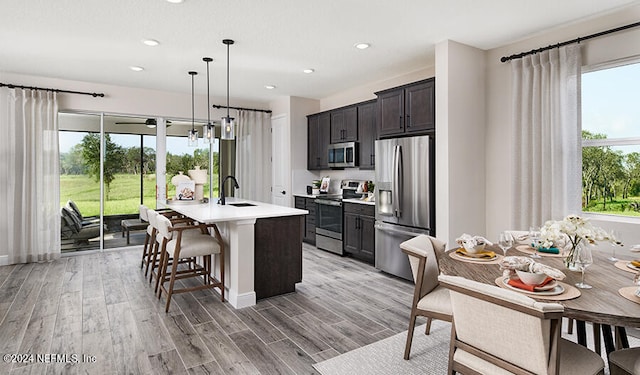 kitchen featuring light wood-type flooring, a center island with sink, appliances with stainless steel finishes, and hanging light fixtures