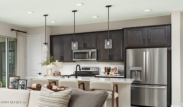 kitchen with appliances with stainless steel finishes, hanging light fixtures, a breakfast bar, tasteful backsplash, and dark brown cabinetry