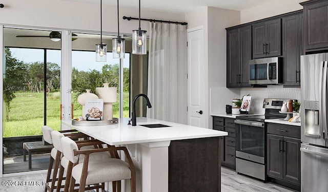 kitchen with hanging light fixtures, sink, a center island with sink, stainless steel appliances, and light hardwood / wood-style floors