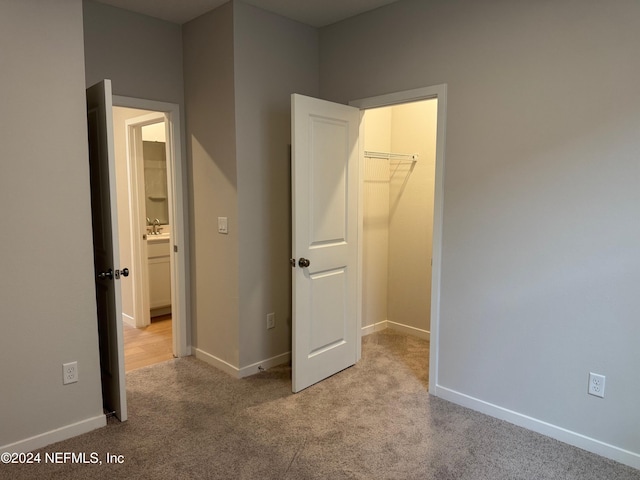 unfurnished bedroom featuring a walk in closet, light colored carpet, and a closet