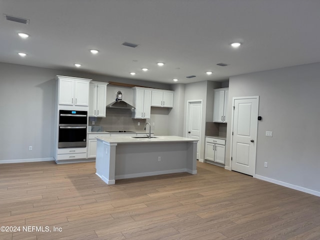 kitchen with white cabinets, wall chimney range hood, sink, and an island with sink