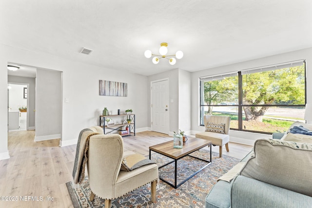 living room with light wood-style floors, baseboards, visible vents, and a notable chandelier