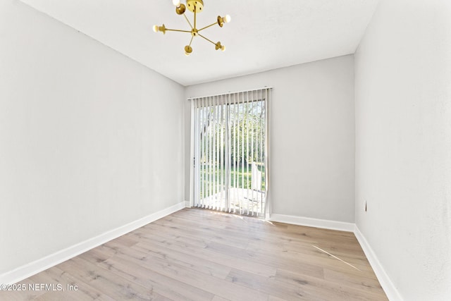 spare room with baseboards, light wood-style flooring, and a notable chandelier