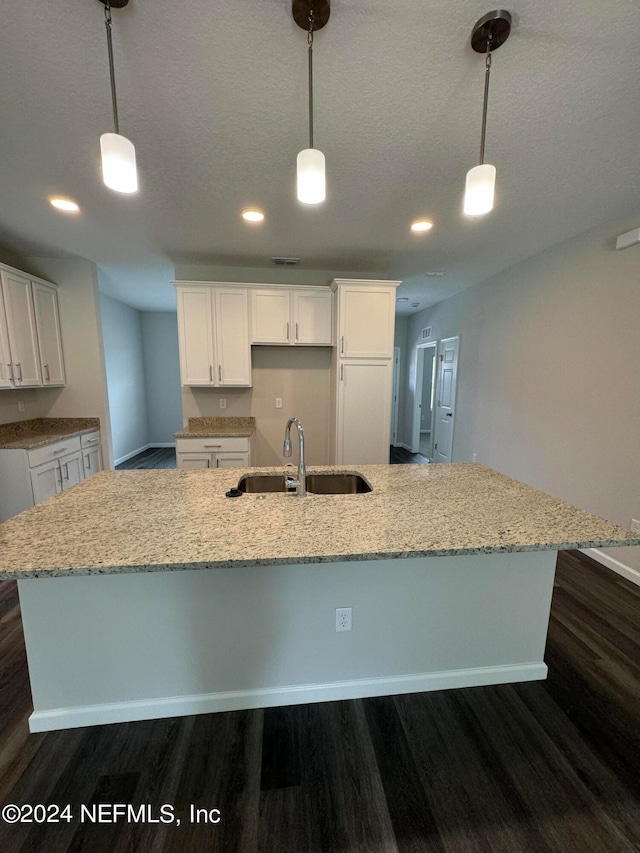 kitchen with an island with sink, decorative light fixtures, dark wood-type flooring, and sink