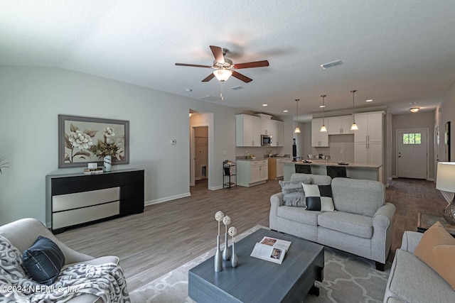 living room featuring a textured ceiling, light hardwood / wood-style floors, vaulted ceiling, and ceiling fan