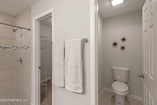 bathroom with a textured ceiling, tile patterned flooring, toilet, and tiled shower