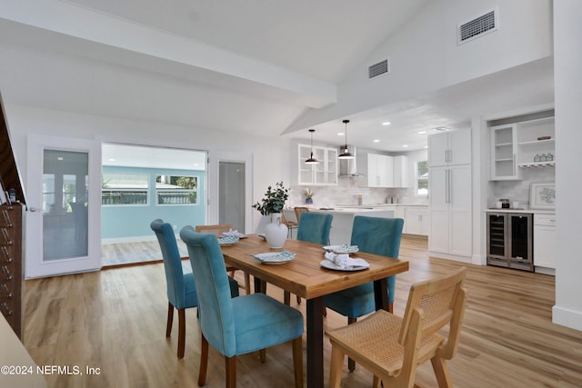 dining area featuring beverage cooler, light wood-type flooring, and vaulted ceiling