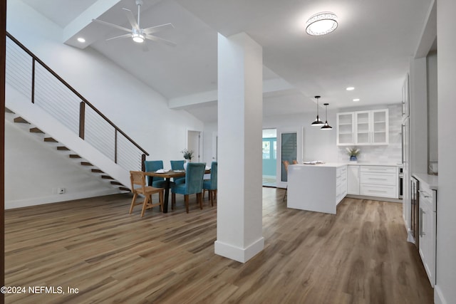 kitchen featuring wood-type flooring, white cabinets, kitchen peninsula, backsplash, and decorative light fixtures