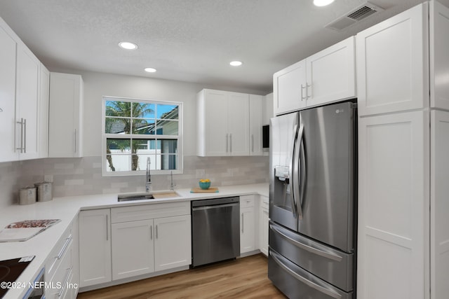 kitchen with stainless steel appliances, light hardwood / wood-style floors, white cabinetry, and sink