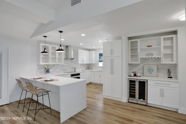 kitchen with light hardwood / wood-style floors, kitchen peninsula, white cabinets, wall chimney range hood, and pendant lighting