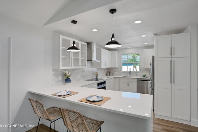 kitchen featuring stainless steel appliances, light wood-type flooring, white cabinetry, kitchen peninsula, and wall chimney exhaust hood