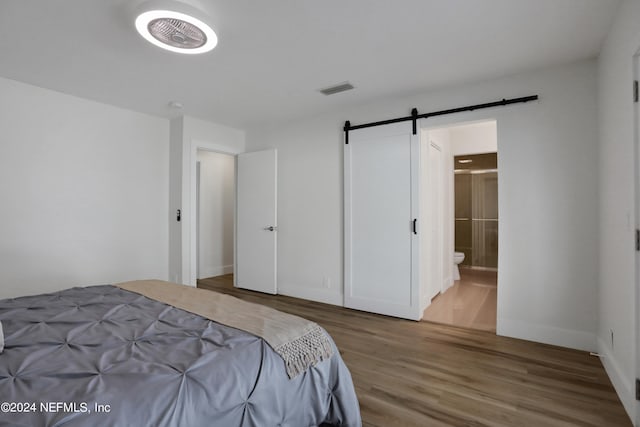 bedroom featuring ensuite bath, a barn door, and hardwood / wood-style flooring